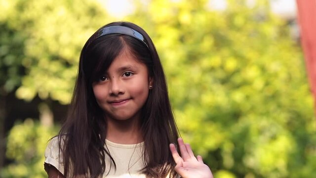 8 year old little girl saying hi with her hand on green bokeh background