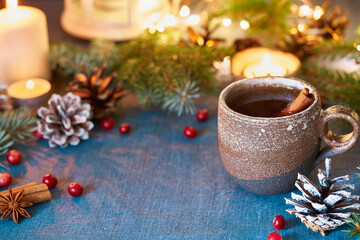 Cup of hot drink on christmas background. Cozy evening, mug of mulled wine, xmas decorations, candles and lights garlands. Dark blue backdrop with glitter and copy space