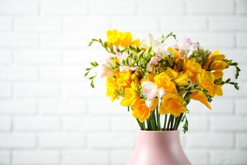 Beautiful blooming freesias in vase against white brick wall. Space for text