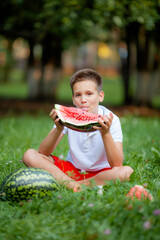 12 year old boy in white t-shirt eating watermelon on the grass in the park