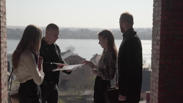 Realtors Real Estate Brokers Talking and Showing Documentation to Potential Buyers Couple of Property in Progress on Open Area.