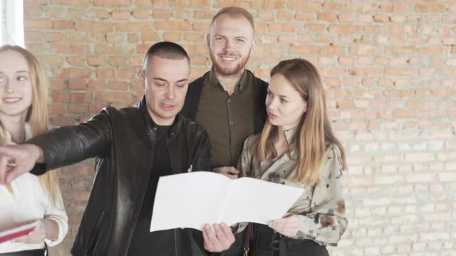 Realtors Real Estate Brokers Holding a Plan of Building and Explains Rooms Arragement to Potential Couple Buyers. Light Camera Movement
