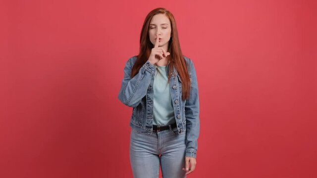 Young red with hair woman showing to be quiet with finger, isolated on a red background.