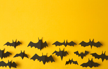 Halloween background. Black bats cut from paper on a yellow background. Halloween decor and decorations for the holiday, copy space.