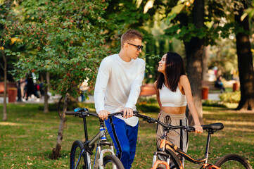 Fototapeta premium Loving young couple standing in an autumn park with bicycles and talking with a smile on their faces. Leisure on bicycles autumn season