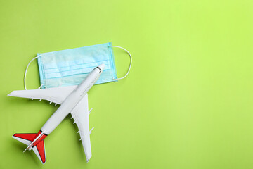 Toy airplane and protective mask on green background, flat lay with space for text. Travelling...