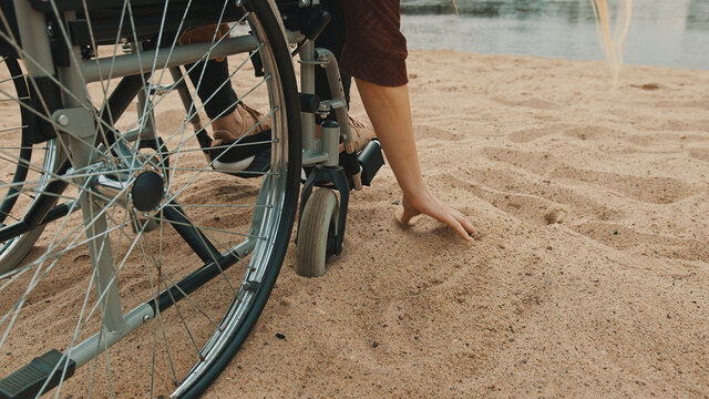 close up, hand of disabled person in the wheelchair playing with the sand on the river coast. Vacation and travel with disability. High quality photo