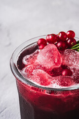 Fresh ice cold fruit cocktail in glass, refreshing summer red currant berry drink with rosemary leaf on stone concrete background, angle view macro