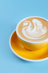 Yellow cup with cappuccino on blue wooden background