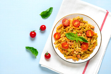 Fusilli - classic italian pasta from durum wheat with chicken meat, tomatoes cherry, basil in tomato sauce in white bowl on blue wooden table Mediterranean cuisine Top view Flat lay