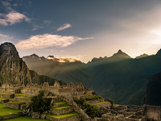 Sunrise with light beams above Machu Picchu overview without people and mountains in background