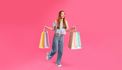 Beautiful young woman with paper shopping bags running on pink background