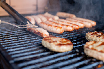 Man at a barbecue grill with smoke.Grilling sausages on barbecue grill. BBQ party.Delicious german sausages or bratwurst .Selective focus.Focus on fork