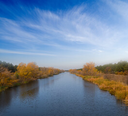 Fototapeta na wymiar irrigation channel with red forest on a coast, autumn river scene
