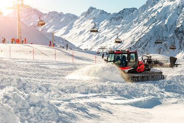 Red modern snowcat ratrack with snowplow snow grooming machine preparing ski slope piste hill at alpine skiing winter resort Ischgl in Austria. Heavy machinery mountain equipment track vehicle