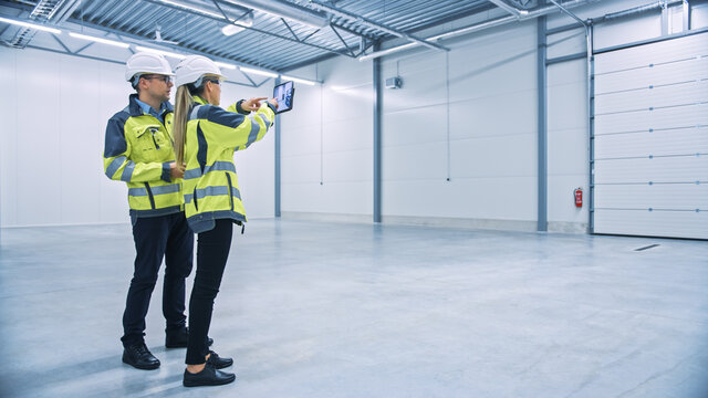 Industry 4.0 Modern Factory: Two Engineers Use Digital Tablet Computer with Augmented Reality Software Visualizing of Manufacturing Plant Room Mapping, Factory Layout. Illustrative Mock-up Concept