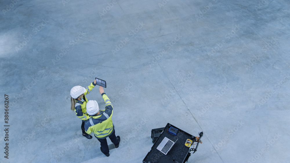 Aufkleber Industry 4.0 Modern Factory: Two Engineers Use Digital Tablet Computer with Augmented Reality Software Visualizing of Manufacturing Plant Room Mapping. Doing 3D Factory Floor Layout. High Angle Shot