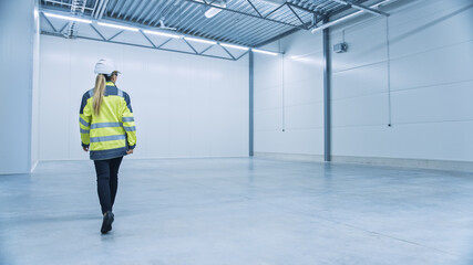 Female Engineer Wearing Safety Hat Walks Across Empty Factory Floor, Inspecting, Planning Machinery...