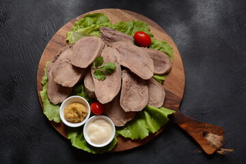 Sliced Beef Tongue Slices on a platter with lettuce leaves, cherry tomatoes and Dijon mustard on a...