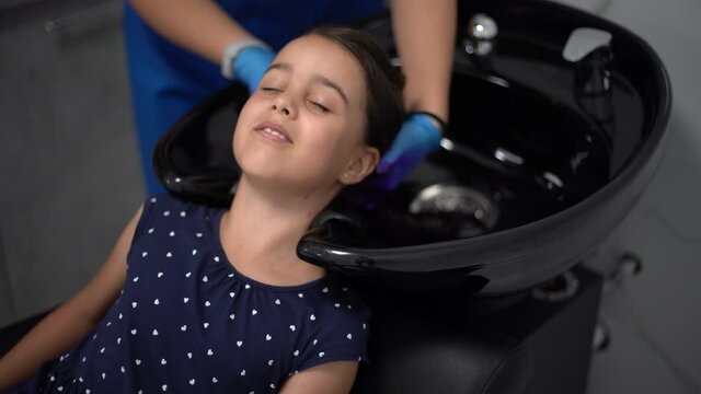 Beautiful little girl looking rubbing her chin choosing air color dye at the beauty salon
