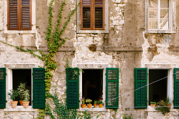 Fototapeta na wymiar An old residential building in cracks with windows and shutters and flowers on the windowsills.