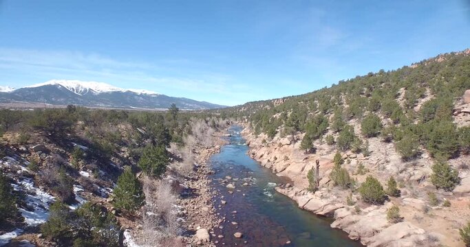 Drone view of a green river in Colorado rocky ground with snowy mountains in the background