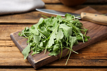 Cutting board with fresh arugula leaves and knife on wooden table, closeup