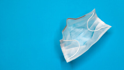 One 3-ply disposable surgical face mask with rubber pads covering the mouth and nose against a blue...