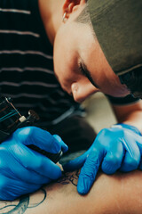 Young tattoo artist tattooing a client's leg.