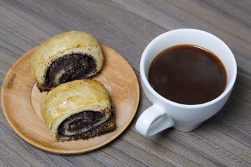 Baked buns with poppy burgers. Lie on a plate. Nearby is a cup of coffee.