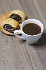 Baked buns with poppy burgers. Lie on a plate. Nearby is a cup of coffee.