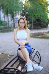 A young woman sits on a bench in the park and throws her legs on the bench.