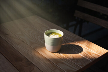 A cup of green tea matcha latte on wooden table at cafe. Healthy food concept. Sun rays. Side view....
