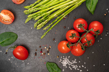 tomatoes on a black board with asparagus with spinach and spices