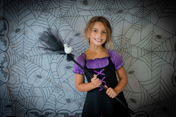funny child girl in witch costume for Halloween over cobweb background