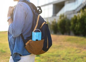 Student holding backpack with medical face mask outdoors.
