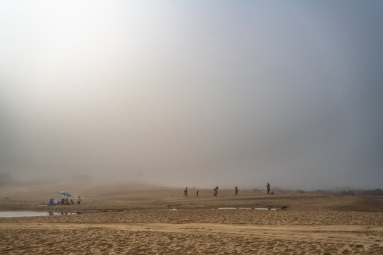 Magische-Mystische Strandlandschaft. Nebel, Fog, Mist, Wolken am Stand mit Menschen in der Distanz und Blick auf den ewigen Ozean.