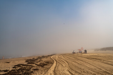 Magische-Mystische Strandlandschaft. Nebel, Fog, Mist, Wolken am Stand mit Menschen in der Distanz und Blick auf den ewigen Ozean.