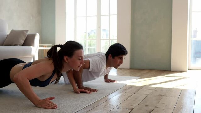 Caucasian man and woman go in for sports indoors. Young girl fooling around with a man while exercising at home. Push-ups with hand claps. Sports concept