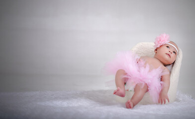 A newborn in a pink dress is sitting in a chair. And there is a blank space for the text