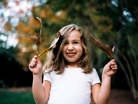 Portrait of a young girl acting goofy with leaves in her hands