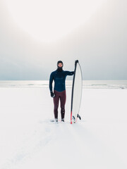 Winter and surfer with surfboard. Snowy beach with surfer in wetsuit.
