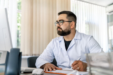 Obraz premium Man sitting at desk. Doctor in scrubs at office near computer. Office in hospital.