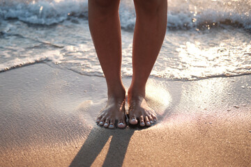 Female feet in the shore of a beach while a wave is coming.