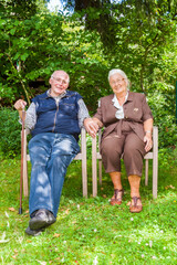 elderly couple sitting hand in hand in their garden
