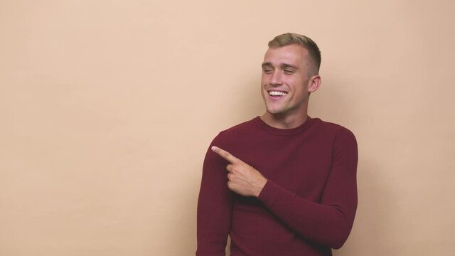 Young caucasian man smiling and pointing aside, showing something at blank space