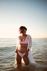 Fototapeta na wymiar Sexy beautiful latin girl having a bath on a deserted beach wearing a pink bikini and pink sunglasses