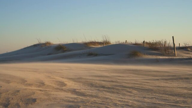 Heavy winds bury a fence under white sand dunes during a sandstorm in the day