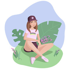 Young smiling girl in baseball cap sitting in the grass with pink and violet flowers in her hand