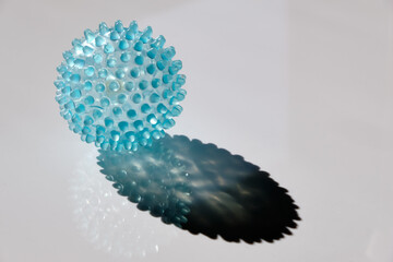 Bright blue transparent massage ball lying in the sun on a plain white background and looking like a virus. Seen in Germany in September.